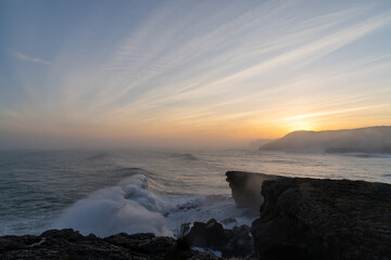 huge storm surge ocean waves crashing onto shore and cliffs at sunrise