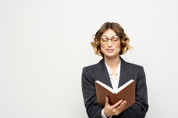 Woman at work with book in hand light background classic suit glasses head