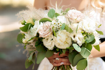 delicate wedding bouquet with white and pink peonies and roses in the hands of the bride. without a face. Outdoors.