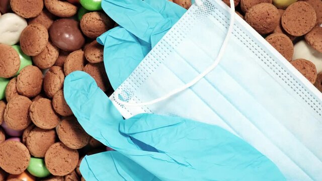 Overhead shot of Dutch holiday Sinterklaas Saint Nicholas day during covid-19 pandemic in the Netherlands with kruidnoten cookies, traditional sweets and medical protective equipment. Rotating