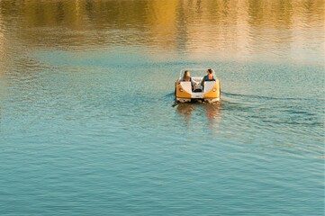 A man and a girl ride a catamaran on a pond. Sunny autumn day.