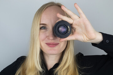 A woman tries on a camera lens instead of an eye. The concept of the photographer's work and the...