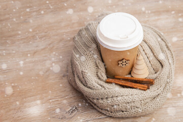 paper cup of coffee wrapped in a santa hat on a white and wooden christmas background.