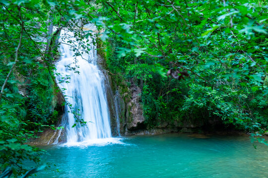 A large beautiful waterfall in a forest with blue water and a trees.