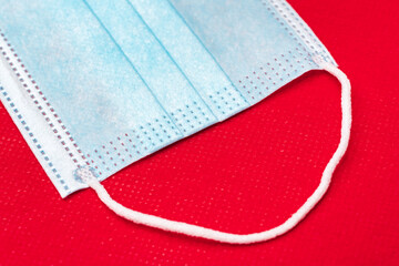 Fragment of blue medical face mask on bright red background of non-woven fabric. Close-up view of medicine concept coronavirus pandemic covid-19 disease, quarantine, global lockdown.