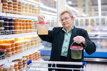 mature woman with glasses chooses pickled vegetables in the supermarket department