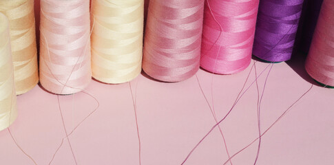  Multi-colored spools of sewing thread on a pink background. Copy space for text. Horizontal format.