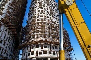 Fototapeta na wymiar Part of a construction machine (excavator or crane) with multi-storey building under construction with scaffolding (new residential complex) on the background, Moscow, Russia