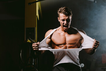 powerful man tearing shirt. Bodybuilder man pumping muscles and ripping shirt in gym. Hot and handsome man tearing shirt with anger and furious. Fitness motivation background