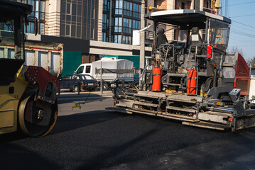 Industrial asphalt paver machine laying fresh asphalt and a Heavy road roller with vibration roller compactor press new hot asphalt on a road construction site.