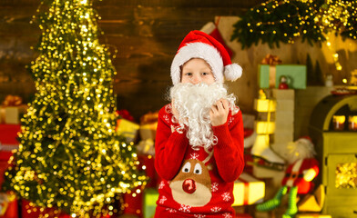 Fototapeta na wymiar Best wishes. santa kid in hat and sweater. winter christmas holiday. buying gifts and presents. seasonal shopping. small boy ready for new year party. happy child celebrate xmas in decorated home