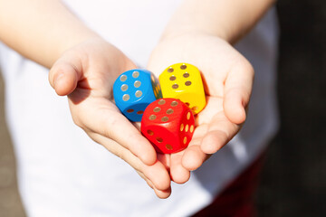Little child holding three colorful wooden dice showing six in her small hands, closeup. Multi colored game dice with number 6 on them. Fortune, success, winning throw luck abstract concept, good odds