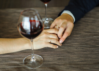 Hands of lovers with wedding rings on the table with glasses of red wine