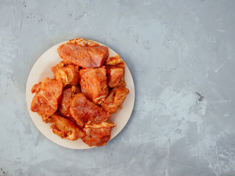 Raw turkey in a marinade with spices on a friendly disposable plate. Marinated chicken for grill and bbq. Raw spiced meat for shish kebab on grey concrete background. Top view. Free space for text.