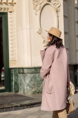 beautiful caucasian brunette woman in a stylish outfit walking down the street in the offseason in a coat and hat
