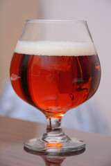 Glass of dark amber beer on a thin stem, on the table close-up