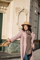 beautiful caucasian brunette woman in a stylish outfit walking down the street in the offseason in a coat and hat
