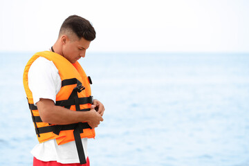 Handsome male lifeguard putting on life vest near sea