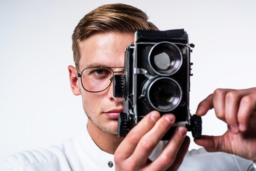 Young photographer in glasses capture image looking in eye of retro camera isolated on white, shoot