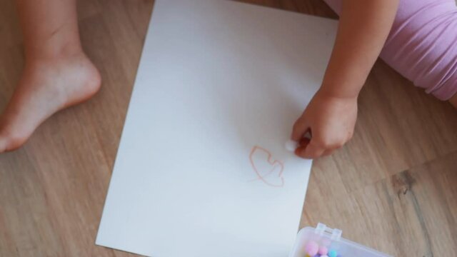 Little girl sitting on the floor and pacing cotton balls on a paper sheet