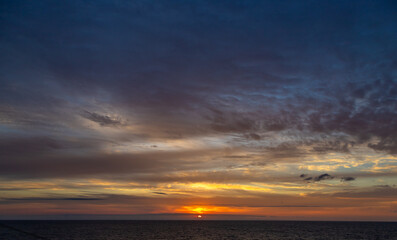 Sunset and dramatic set of clouds drifting over the tropical waters of the Caribbean Sea are lit by the last moments of daylight.
