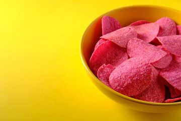 Obraz na płótnie Canvas Pink potato chips in a plate on a yellow background, side view