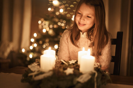 Child sits alone in front of a glowing Advent wreath and looks forward to Christmas. Girls, candles, warm