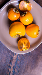 Persimmon cut into slices and halves of persimmon on a plate on a wooden table, close-up, copy space