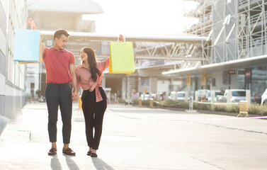 Happy young couple of shoppers walking in the shopping street towards and holding colorful shopping bags in hand. Concept of sale and black friday shopping