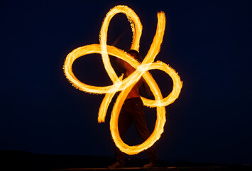 Solo fire artist perform infinite spirals by spinning flaming pois on dark sky at night outdoors,...