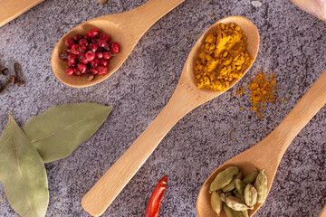 Different spices on stone background. Cardamom, turmeric, pink pepper, chili pepper, bay leaf, clove. Horizontal direction. Flat lay.