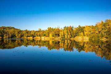 A beautiful little lake called Schnepfensee in Germany at a sunny day in Autumn with a colorful forest reflecting in the water.