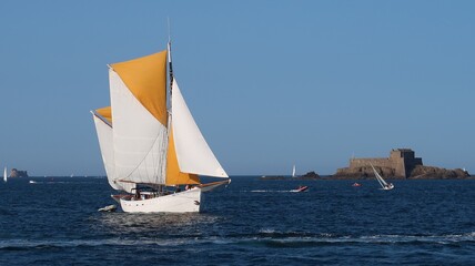 Voilier ancien naviguant sur la mer, dans la baie de Saint-Malo en Bretagne, au large de l’île du fort du Petit Bé (France)