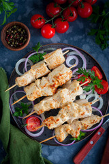 Chicken skewers on wooden skewers with vegetables on a ceramic plate, selective focus
