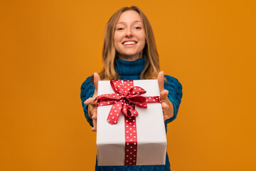 Cheerful young womanis showing present box to camera. Focus on gift box. Studio shot, yellow background.