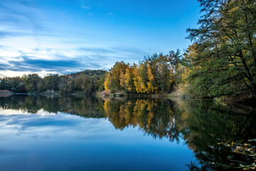 Fototapeta na wymiar A beautiful little lake called Schnepfensee in Germany at a sunny day in Autumn with a colorful forest reflecting in the water.