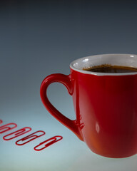 red cup with coffee and red paper clips lie on a light background.