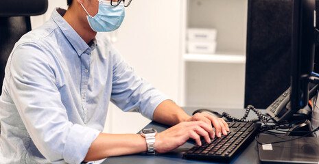 Young asian man using laptop computer working and video conference meeting online chat in quarantine for coronavirus wearing protective mask with social distancing at home.work from home concept