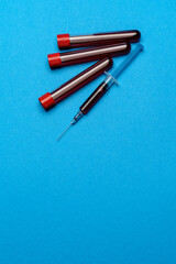 Syringe And Plastic Test Tube With Blood Sample over blue background with copyspace