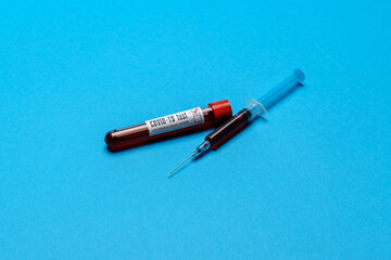 Syringe And Plastic Test Tube With Blood Sample over blue background with copyspace
