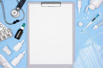 Fototapeta na wymiar Blank patient medical history, stethoscope, digital thermometer, face masks, cold and flu treatment medications on blue desk. Medicine mock-up background with copy space