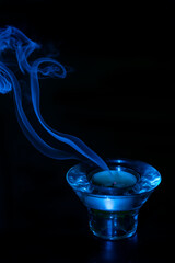 Blue glass candle holder with dark background and with smoke coming out of the candle after being...