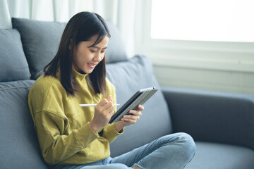 An Asian woman sitting on a tablet on a sofa