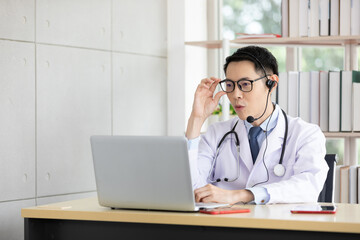 asian doctor talking with patient or co-worker through online video chat with computer in hospital
