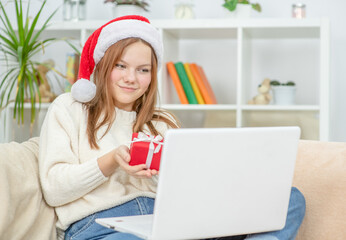 Happy Teen girl meets Christmas (New Year) through a video call with friends during pandemic coronavirus and shows gift box