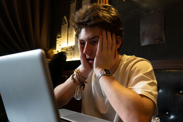 Young man sitting at a table with a laptop, very scared and afraid hidden