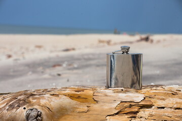 Hip flask on a wooden beam lying on the beach. - obrazy, fototapety, plakaty