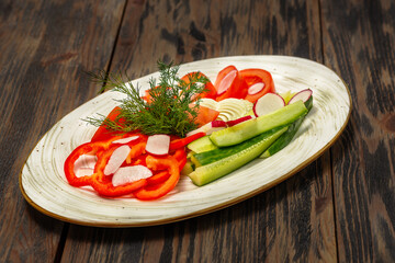 Tomato and cucumber salad with greens on a white plate on a wooden background