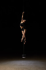 Beautiful young pole dancer woman on pylon isolated on black background.