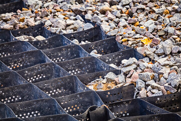 Cellular confinement system - plastic black honeycomb frame filled with small natural stones closeup. Used in construction for erosion control, soil stabilization on flat ground and steep slopes